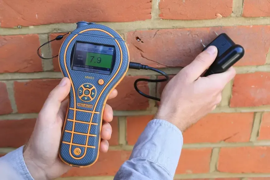 A moisture meter pressed against a brick wall to check how far water spread after a leak